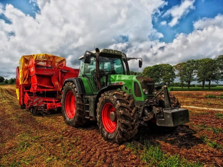 En grön traktor på en åker med molnig himmel i bakgrunden.